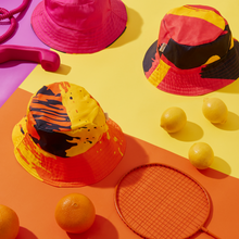 Load image into Gallery viewer, Reversible bucket hats featuring fun bold patterns, made with cotton drill and a layer of infusible fabric. Vibrant colors on the inside. A stylish accessory for festivals and outdoor events.p with lemons oranges and a racket
